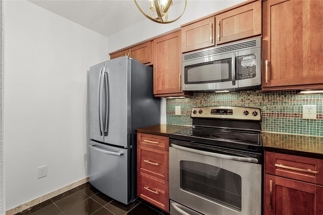 kitchen featuring dark tile patterned floors, baseboards, appliances with stainless steel finishes, tasteful backsplash, and dark countertops