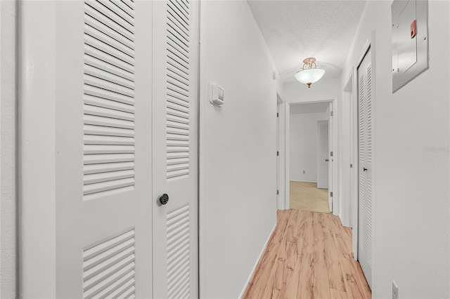 hall with a textured ceiling, light wood-style flooring, and baseboards