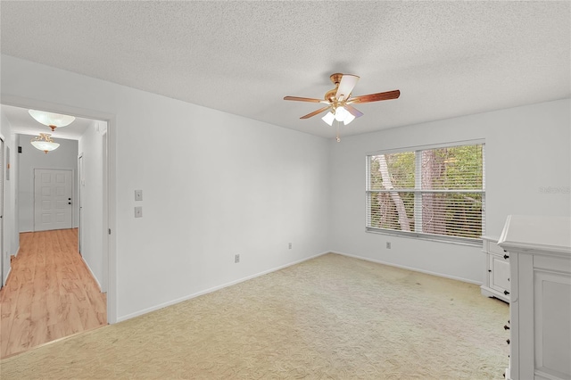 unfurnished room with light carpet, baseboards, a ceiling fan, and a textured ceiling