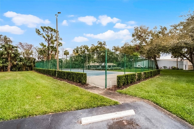 view of tennis court with fence and a lawn