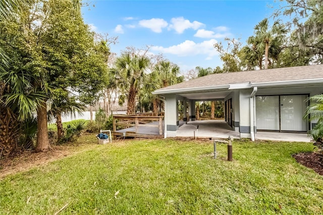 rear view of house with a shingled roof, a lawn, and a patio area