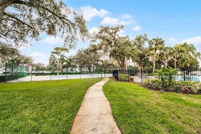 view of community with a tennis court, a yard, and fence