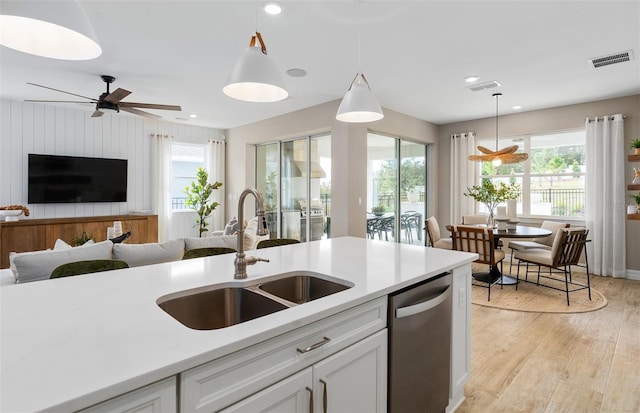 kitchen with pendant lighting, sink, white cabinetry, light hardwood / wood-style floors, and stainless steel dishwasher