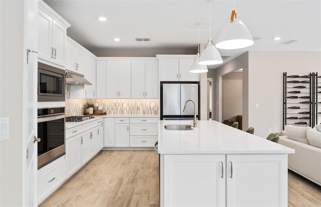 kitchen featuring appliances with stainless steel finishes, pendant lighting, sink, white cabinets, and a kitchen island with sink