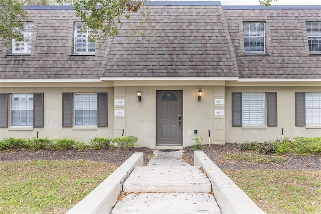 view of front of property with stucco siding, mansard roof, and roof with shingles