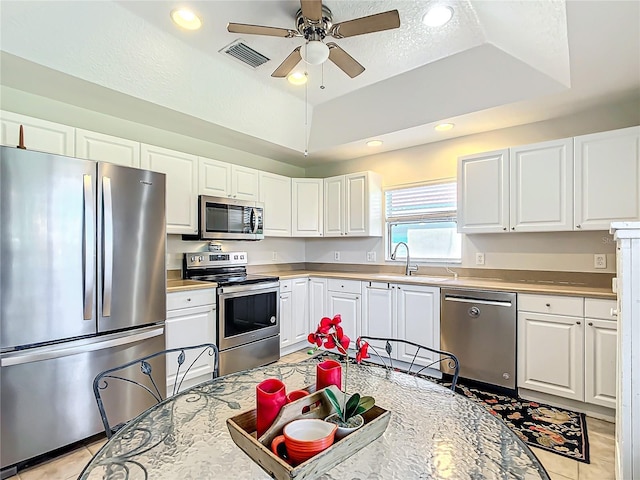 kitchen with a raised ceiling, stainless steel appliances, and white cabinetry