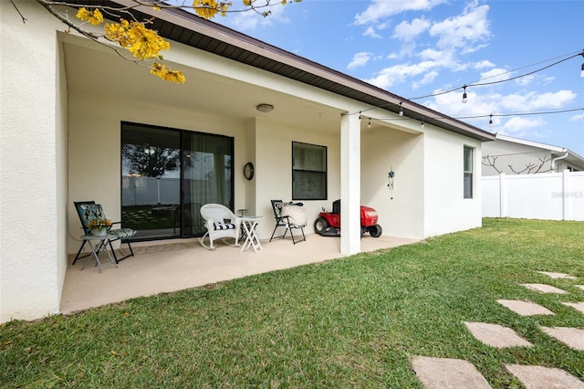 back of property featuring stucco siding, a patio area, fence, and a yard