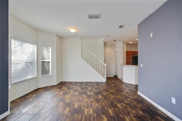 empty room featuring stairway, dark wood finished floors, visible vents, and baseboards