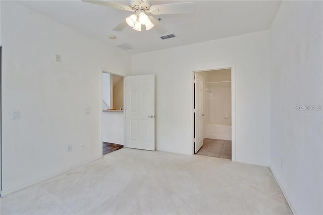 unfurnished bedroom featuring light carpet, ensuite bath, ceiling fan, and visible vents