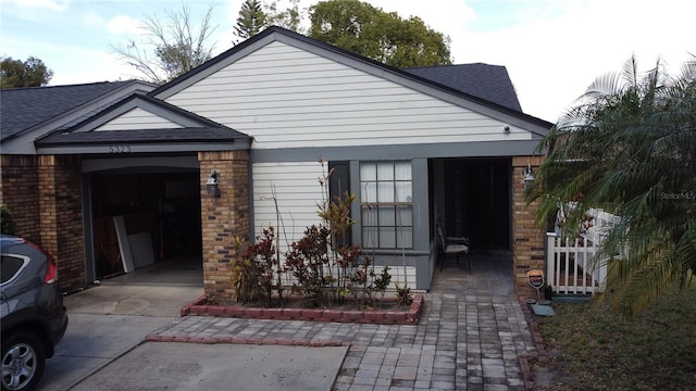 exterior space featuring driveway, an attached garage, a shingled roof, and brick siding