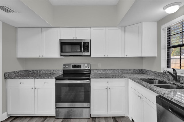 kitchen with stainless steel appliances, white cabinets, stone counters, hardwood / wood-style floors, and sink