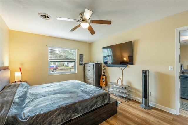 bedroom with a ceiling fan, visible vents, baseboards, and wood finished floors