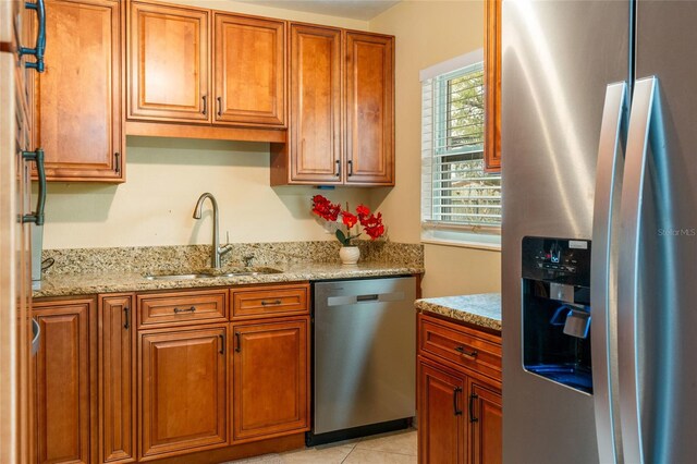 kitchen featuring stainless steel appliances, brown cabinetry, a sink, and light stone countertops