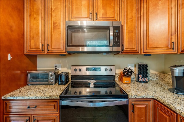 kitchen featuring light stone countertops, electric range, stainless steel microwave, and brown cabinetry