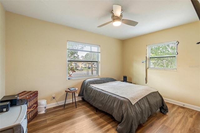 bedroom featuring multiple windows, ceiling fan, baseboards, and wood finished floors