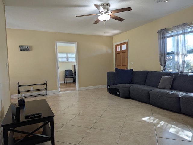 living area with light tile patterned flooring, ceiling fan, a wealth of natural light, and baseboards
