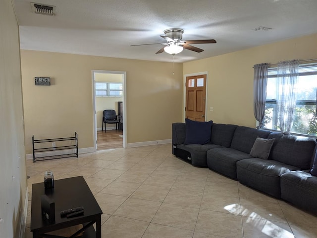 living area with light tile patterned floors, visible vents, ceiling fan, and baseboards