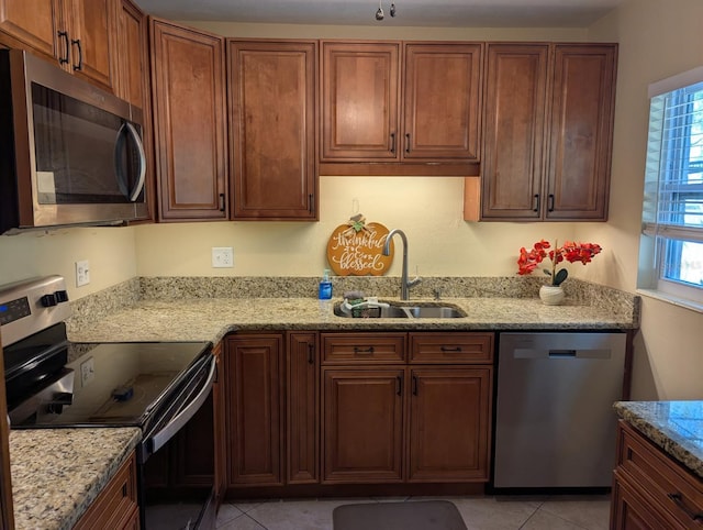 kitchen featuring light tile patterned floors, light stone counters, a sink, and appliances with stainless steel finishes