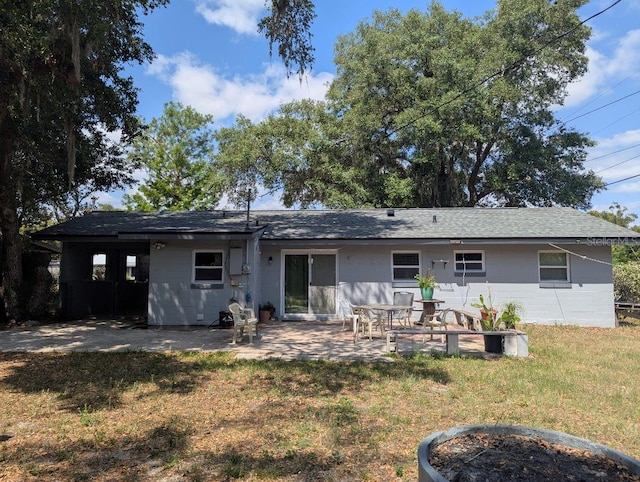 rear view of house featuring a patio, a yard, concrete block siding, and roof with shingles