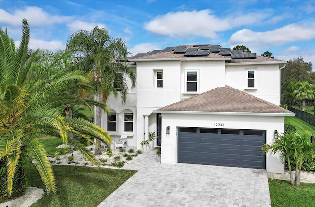 view of front facade with decorative driveway, roof mounted solar panels, an attached garage, and stucco siding