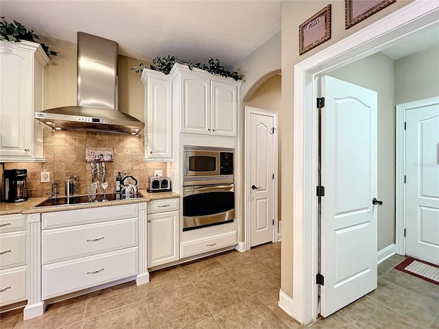 kitchen with white cabinetry, tasteful backsplash, light tile patterned floors, appliances with stainless steel finishes, and wall chimney exhaust hood