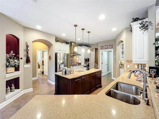 kitchen with appliances with stainless steel finishes, dark brown cabinets, wall chimney range hood, decorative light fixtures, and sink