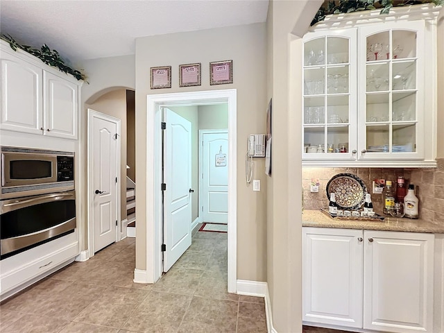 kitchen with appliances with stainless steel finishes, light tile patterned floors, tasteful backsplash, and white cabinets