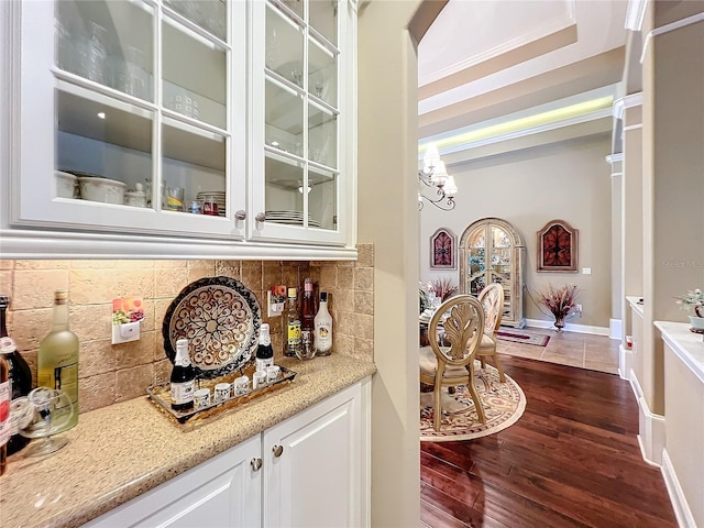 bar featuring a chandelier, white cabinetry, dark hardwood / wood-style flooring, light stone countertops, and decorative backsplash