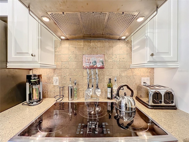 kitchen featuring backsplash, black electric cooktop, light stone counters, custom exhaust hood, and white cabinets