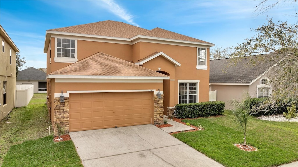 traditional home featuring concrete driveway, stone siding, stucco siding, an attached garage, and a front yard