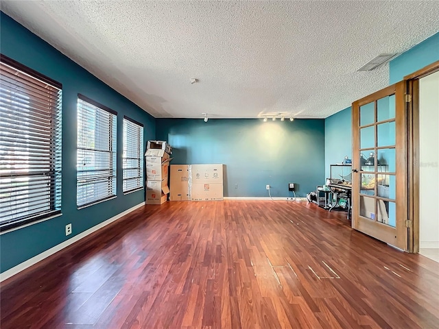 unfurnished room with rail lighting, a textured ceiling, baseboards, and wood finished floors