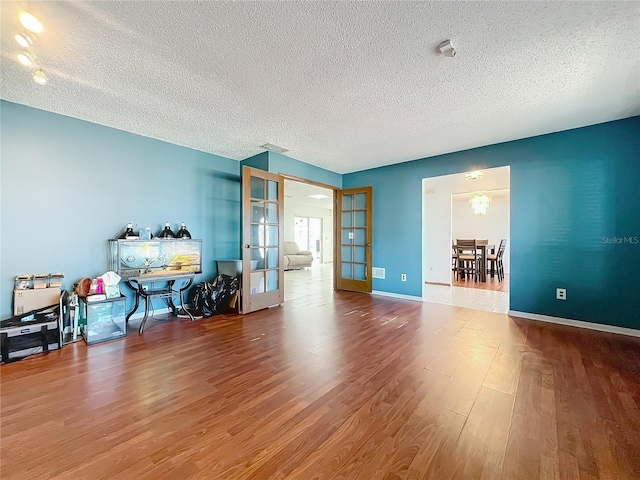 spare room with a textured ceiling, baseboards, wood finished floors, and french doors