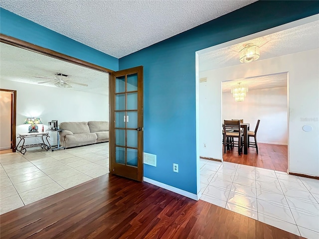 spare room featuring baseboards, visible vents, wood finished floors, a textured ceiling, and ceiling fan with notable chandelier