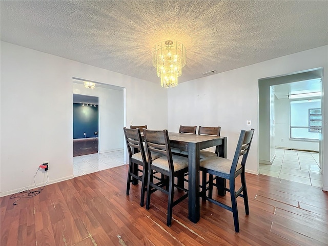 dining room with visible vents, an inviting chandelier, a textured ceiling, wood finished floors, and baseboards