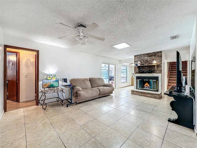 living room featuring light tile patterned floors, visible vents, ceiling fan, a textured ceiling, and a fireplace