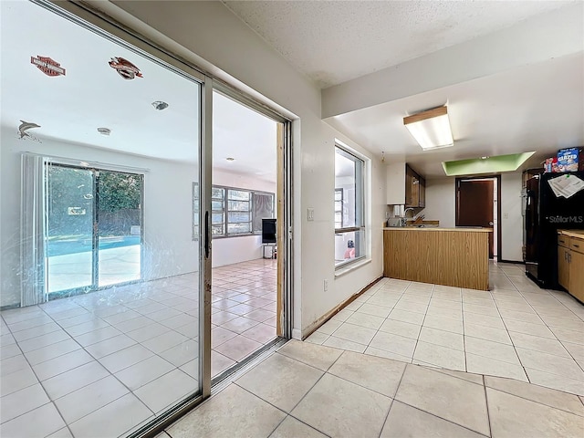 kitchen with light tile patterned floors, a textured ceiling, a peninsula, a sink, and freestanding refrigerator