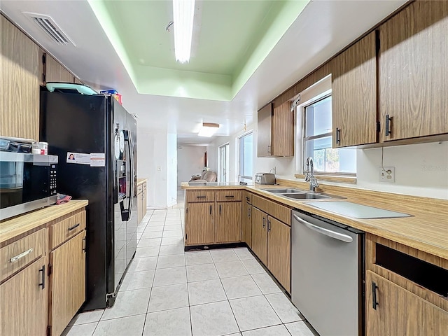 kitchen with light tile patterned flooring, a sink, visible vents, appliances with stainless steel finishes, and a tray ceiling