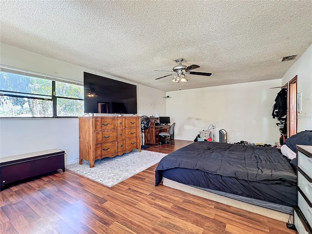 bedroom featuring a ceiling fan, a textured ceiling, visible vents, and wood finished floors