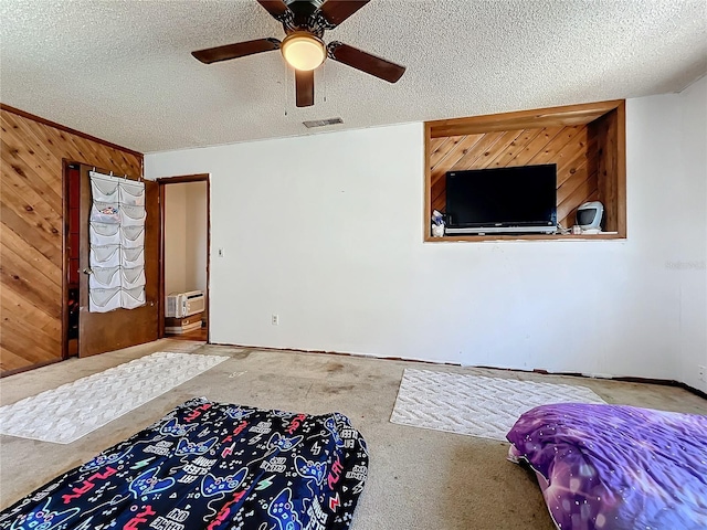 bedroom with carpet floors, visible vents, a ceiling fan, wood walls, and a textured ceiling