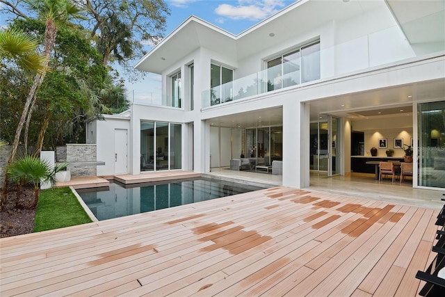 back of house with a balcony, an outdoor pool, and stucco siding