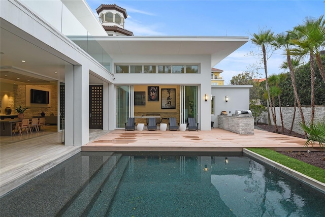 back of property with a fenced in pool, a patio, a wooden deck, and an outdoor kitchen