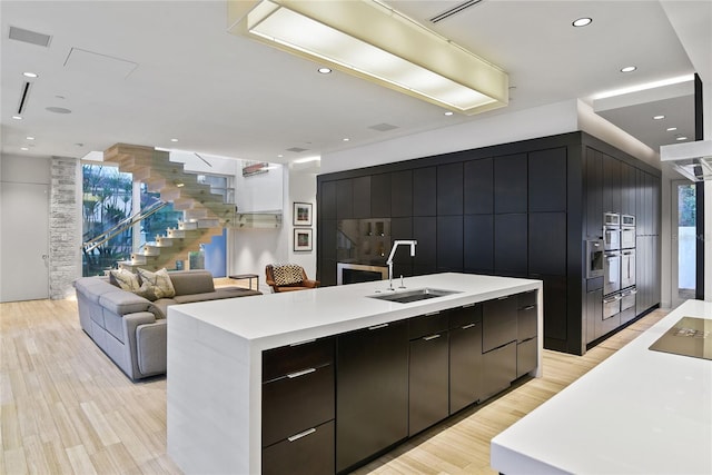 kitchen with a kitchen island with sink, a sink, light countertops, modern cabinets, and open floor plan