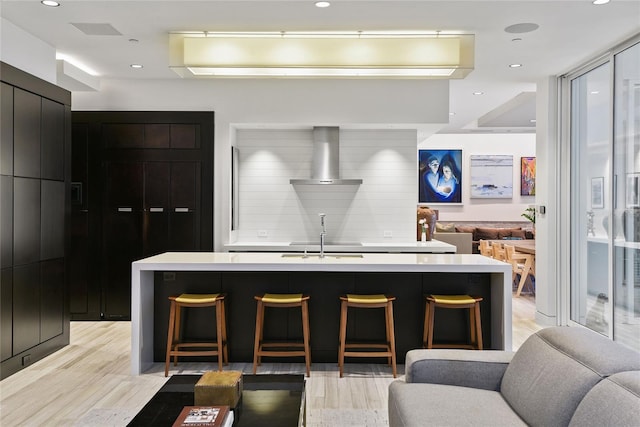 kitchen with a breakfast bar area, light countertops, wall chimney exhaust hood, modern cabinets, and open floor plan