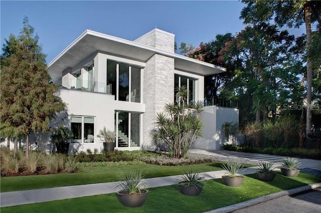 exterior space featuring a yard, a chimney, a balcony, and stucco siding