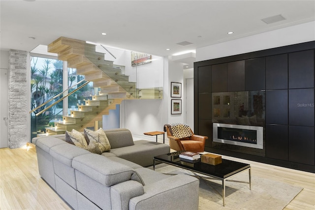 living area featuring recessed lighting, light wood-type flooring, a fireplace, and stairs