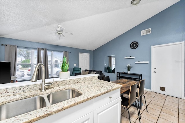 kitchen with light tile patterned floors, white cabinets, ceiling fan, vaulted ceiling, and a sink