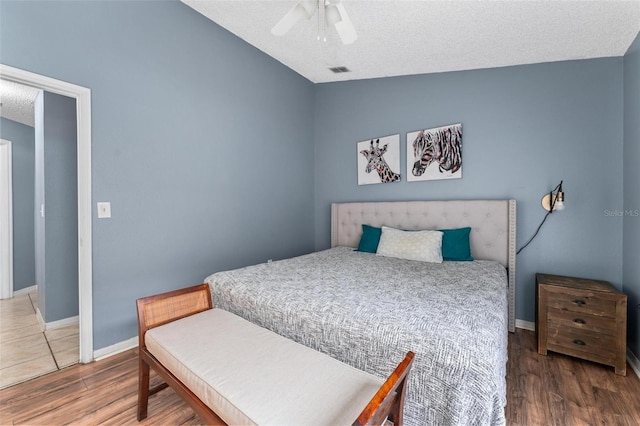 bedroom featuring lofted ceiling, a textured ceiling, baseboards, and wood finished floors