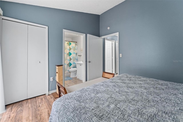 bedroom with light wood-type flooring, connected bathroom, a closet, and lofted ceiling