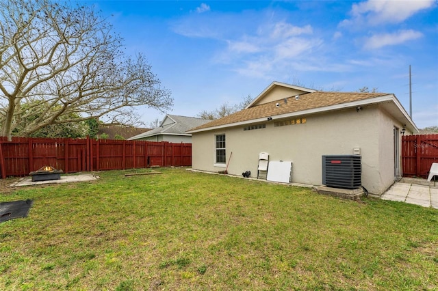 back of property with stucco siding, a lawn, central AC unit, an outdoor fire pit, and a fenced backyard