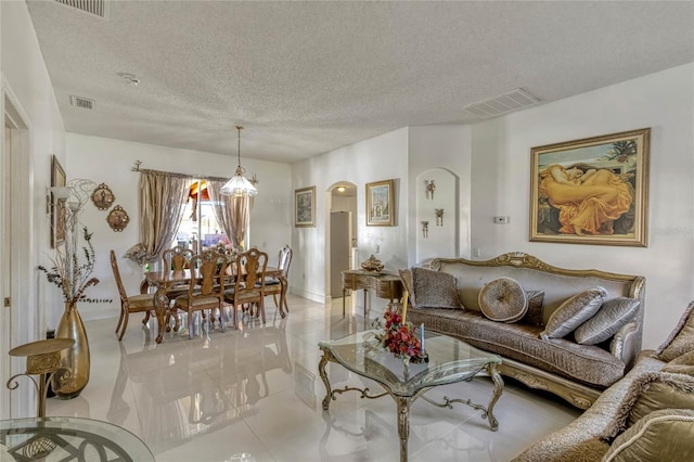 living room featuring a textured ceiling, light tile patterned flooring, arched walkways, and visible vents